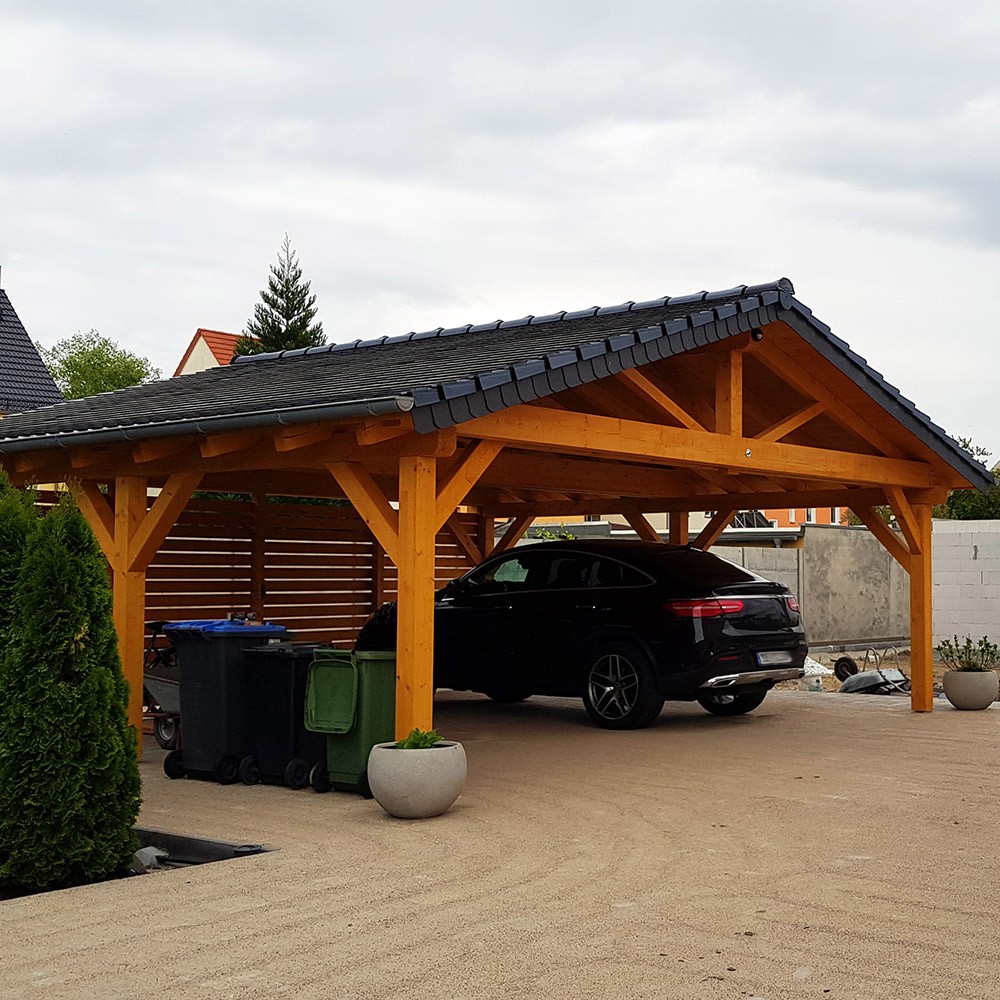 timber carport with a dark shingle roof covering a black car on a paved driveway