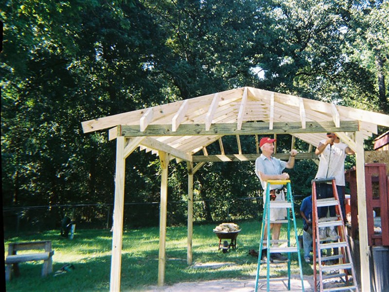 covered carport frame with roof rafters under construction beside a home