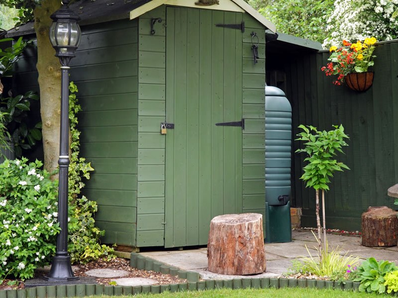 green garden tool shed with wood siding and a small landscaped patio