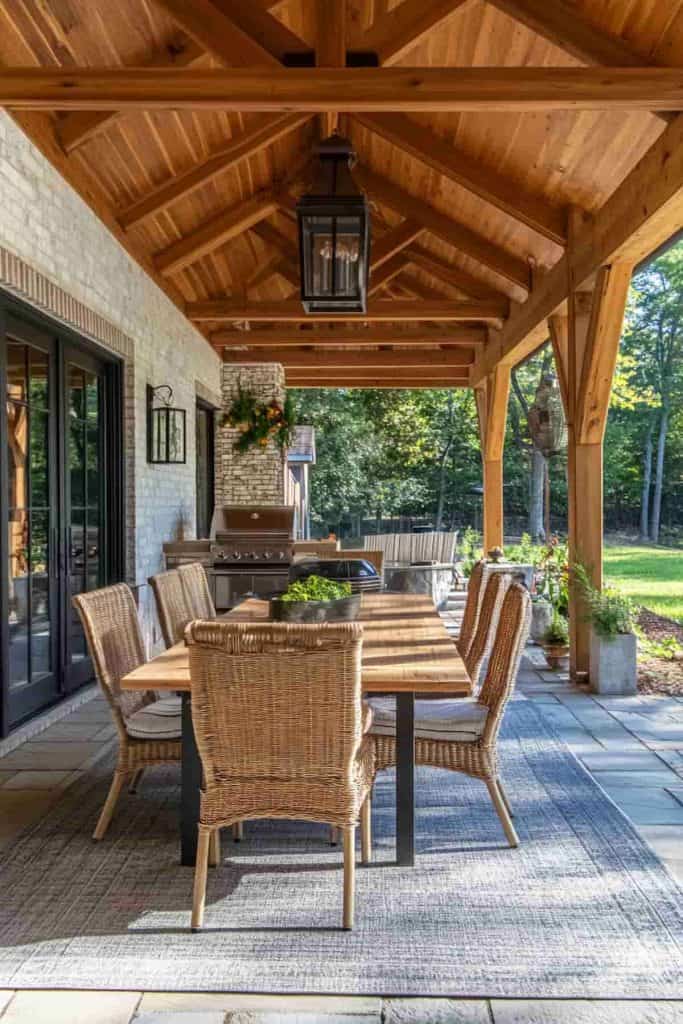 covered patio with a wood vaulted ceiling, timber posts, dining table, wicker chairs, and outdoor grill